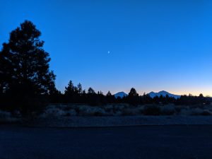 Crescent moon, pine trees, and mountains.
