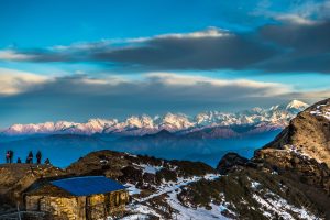 People admiring a snowy mountain range under cloudy skies.