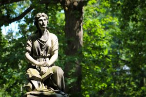 Statue in the woods of an upgazing woman with a book.