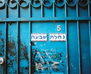 The upper half of a metal blue door with the number 5, and Hebrew text נחלת שבעה.
