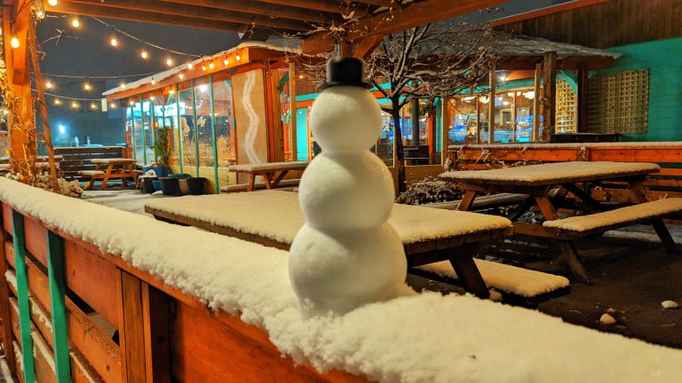 Small snowman on the railing of a restaurant patio in the winter snow.