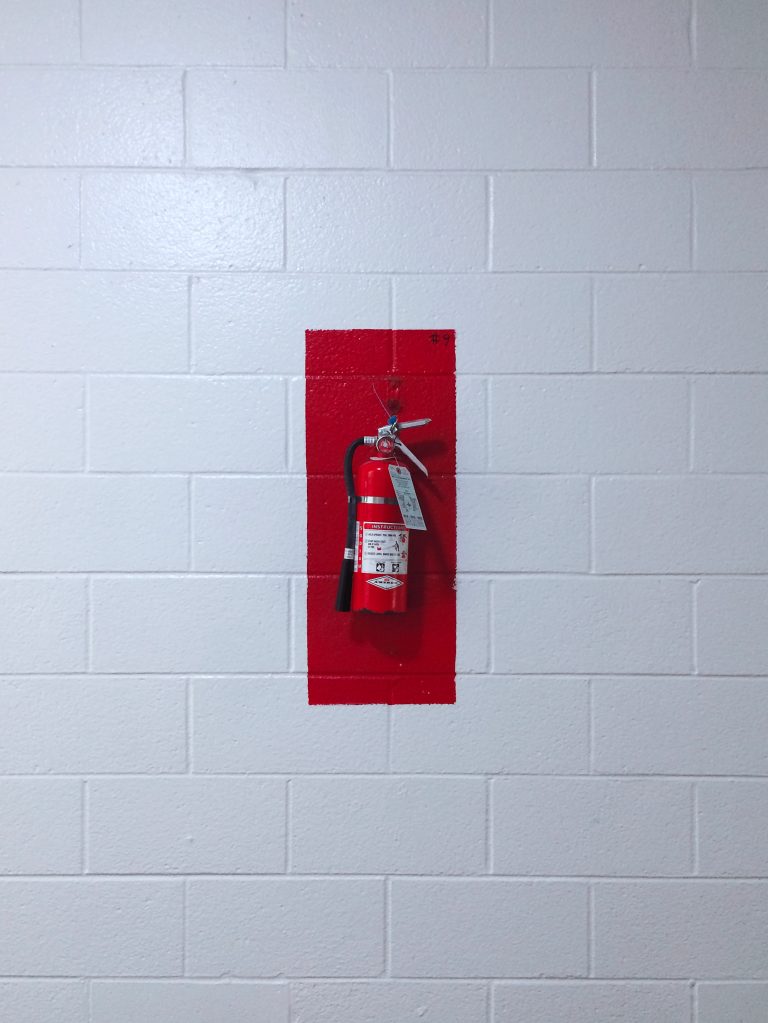 Fire extinguisher with painted red background mounted on a white cinderblock wall.