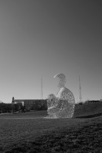 Black and white photo of a statue of a person sitting in a field. 