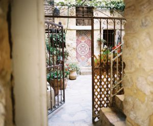 Looking through a gate, into a Jerusalem courtyard with plants and a decorated door.
