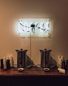 Coffee station on wooden countertop and neon coffee sign above.