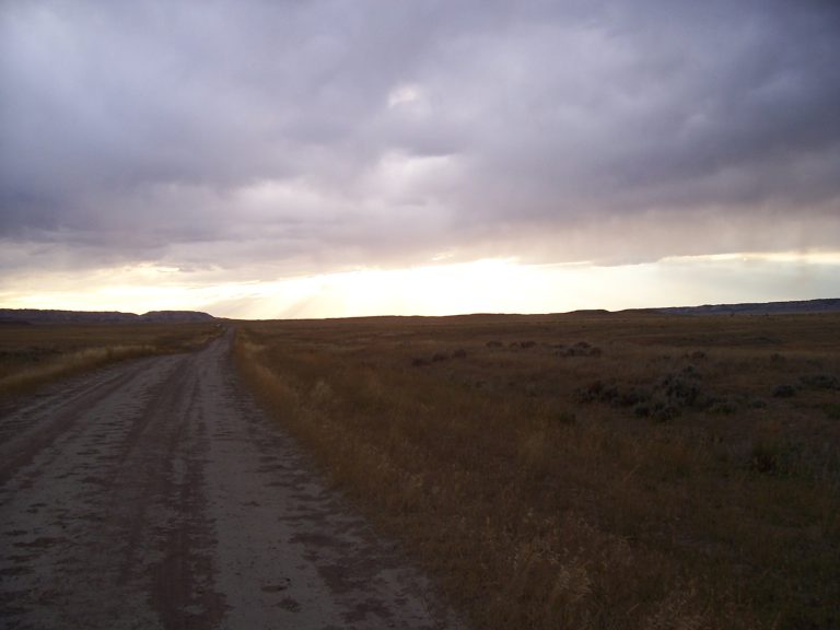 Dusty road across the desert under a cloudy sky