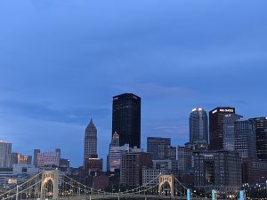 City of Pittsburgh skyline at night in the background, with a yellow bridge in front