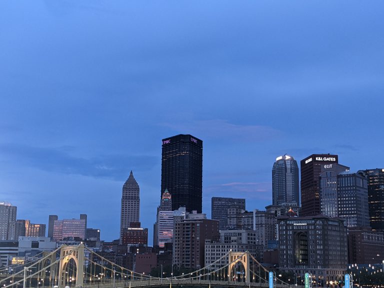 City of Pittsburgh skyline at night in the background, with a yellow bridge in front