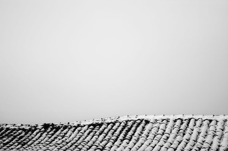 A sagging old tiled roof with a light covering of snow in black and white