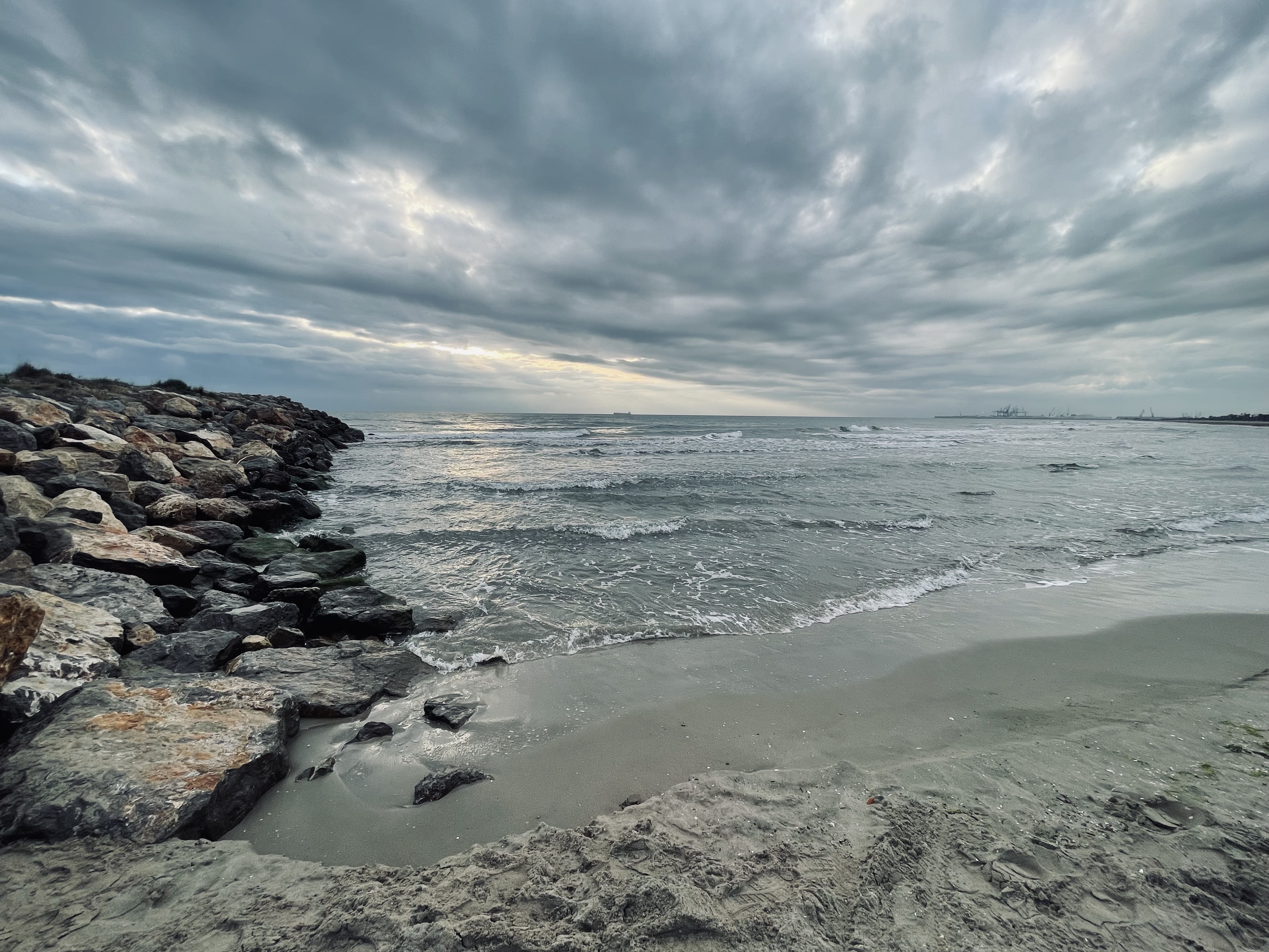 A serene coastal scene with a rocky breakwater on the left, extending into the ocean.