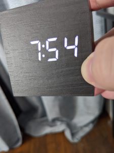 View larger photo: A square digital clock, held in someone's hand. It is 7:54