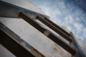 View up a ladder leaning against a wall with the sky above