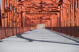 Perspective view of a orange metal bridge and grey deck converging in distance
