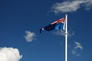 Flag of New Zealand waving in strong wind with white cloud and blue sky.