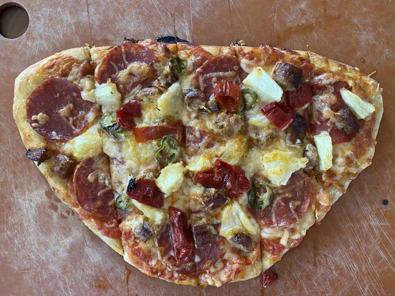 Hand-tossed thin-crust pizza on cutting board, with cheese, pepperoni, sausage, goat horn pepper, pineapple, and jalape?o