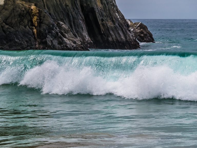 Waves crashing onto shore in California with cliffs in the background