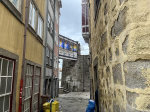 Narrow street near the water in Porto, Portugal. There's a walking bridge above it at the end for people to get from one side to the other.