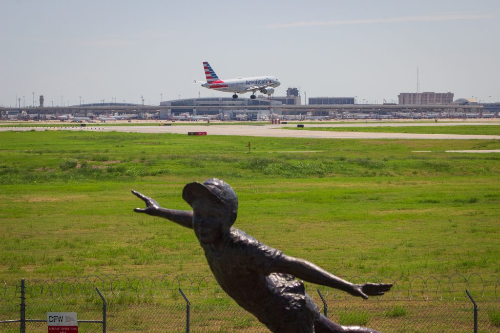 An American Airlines plane landing behind a statue of a young kid