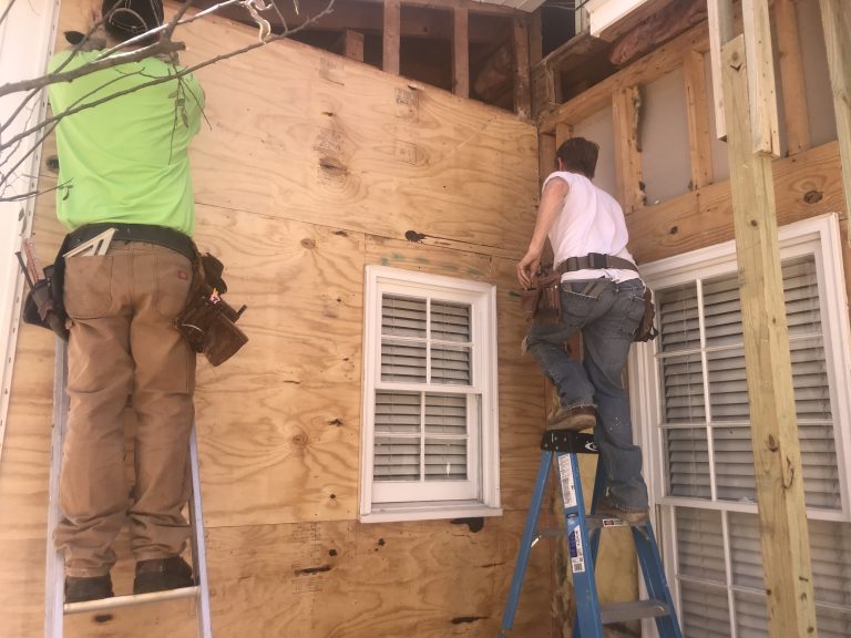 Two people on ladders doing carpentry/building.