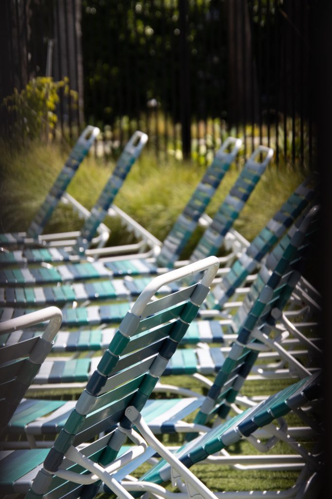 A row of empty pool chairs through a gap in the fence