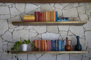 A couple of bookshelves with colorful books on a stone wall
