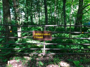 Metal gate at the edge of the woods with a sign "Campground closed". Presqu'ile Provincial Park, Ontario, Canada.