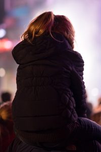 Girl sitting on her parent's shoulders at an outdoor concert