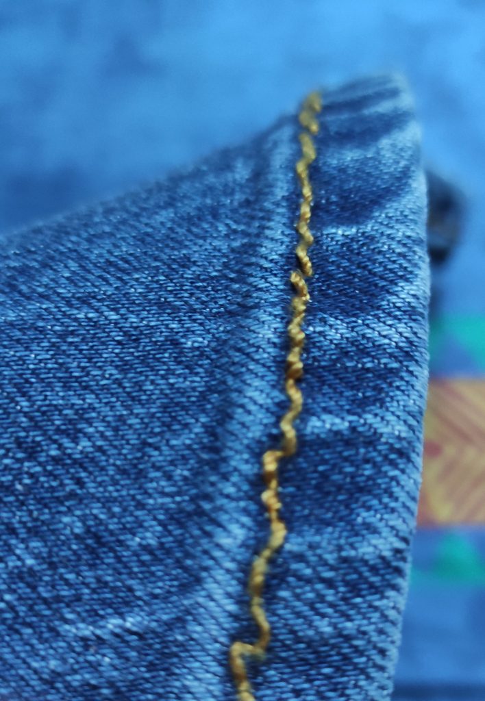 A hem of blue jeans with golden thread