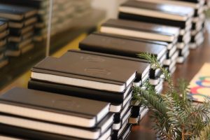 Stacks of black notebooks on a table with evergreen holiday decorations
