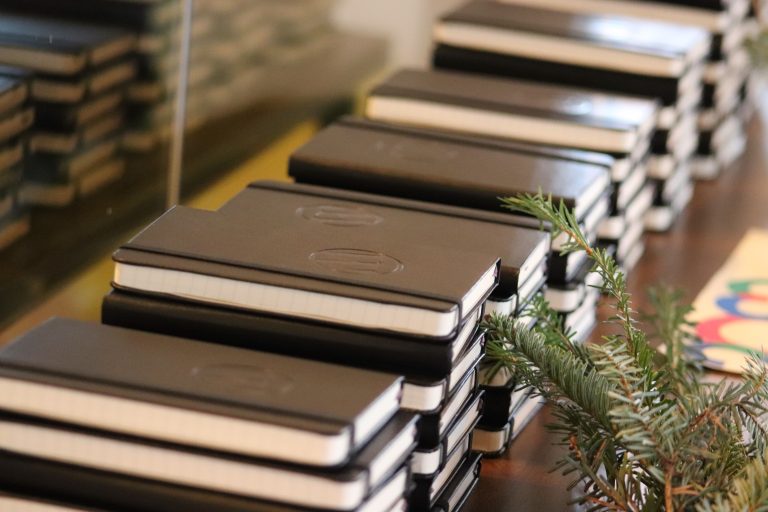 Stacks of black notebooks on a table with evergreen holiday decorations