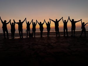 Photo which is about unity of friends, Sunset beach with friends, people in dark stand, people in sunset, people on beach, people hold hand
