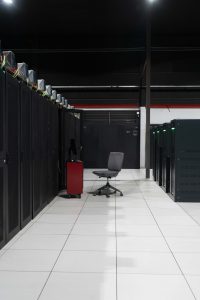 A system administrator’s workstation within a data processing centre with rack cabinets and servers inside.
