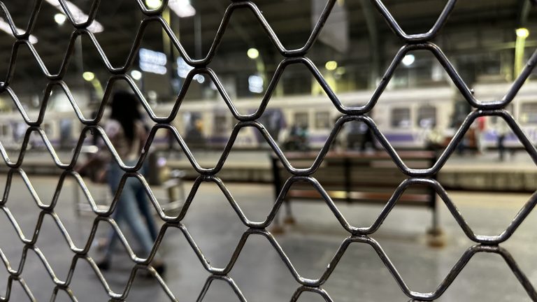 Closeup of a fence with a train yard behind it.