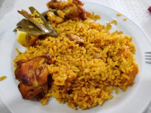 Paella, a dish that’s primarily rice with some chicken on the bone and a little green garnish
