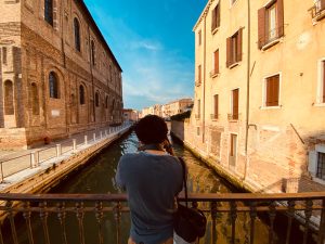 View of a Venetian canal with one person photographing from the bridge
