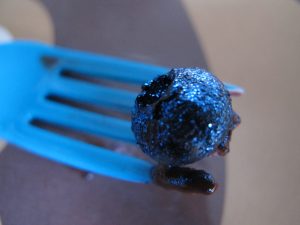A blue plastic fork holding a sparkling blue blueberry.
