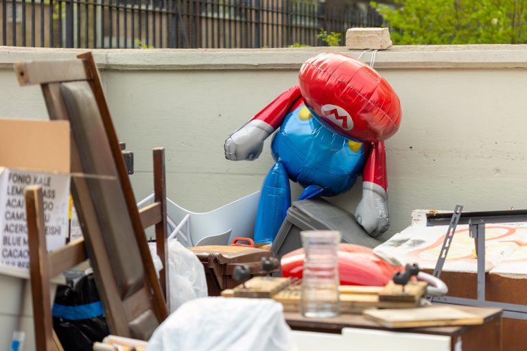 Semi-deflated mario balloon in a trash area.