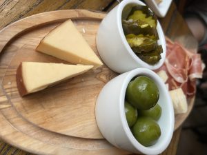 Charcuterie board with smoke gouda, olives, pickles, and thin sliced pork.