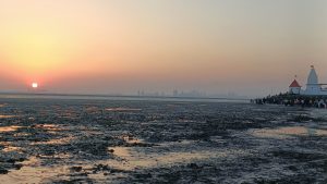 Dramatic Sunset. Looking out over a seabed at low tide, a city on the horizon behind some clouds, the sun just going down.