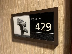 View larger photo: Hotel room door placard. It says Welcome at the top, then room 429. The number is written in braille right under the print, and to the left is a small picture of a mailbox to help people remember their room.