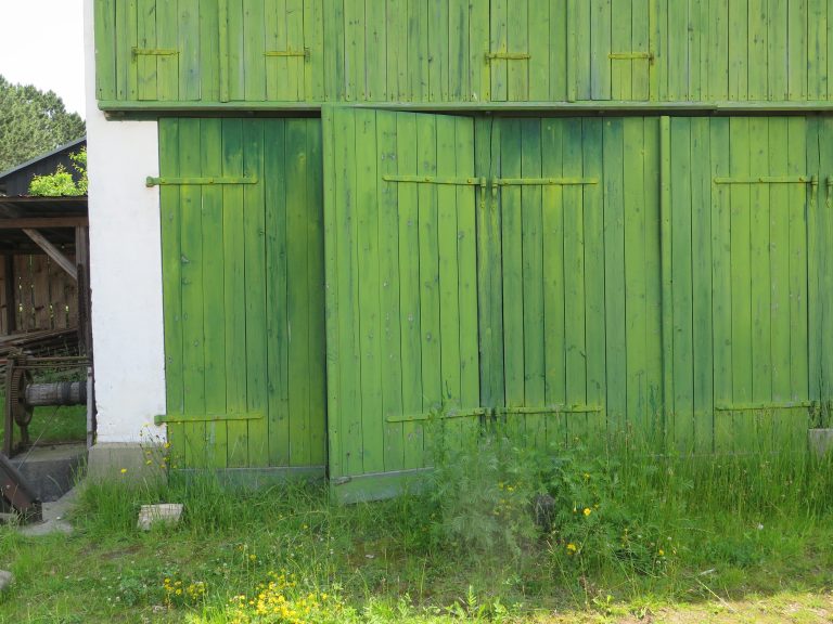 A building with a row of green wooden doors, one of which is slightly open.