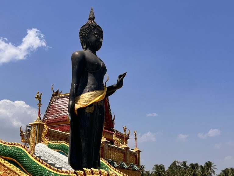 A Buddha statue under a bright blue sky at the entrance of the Wat Baan Ngao temple in Ranong area, thailand. Bhuddism, meditation.