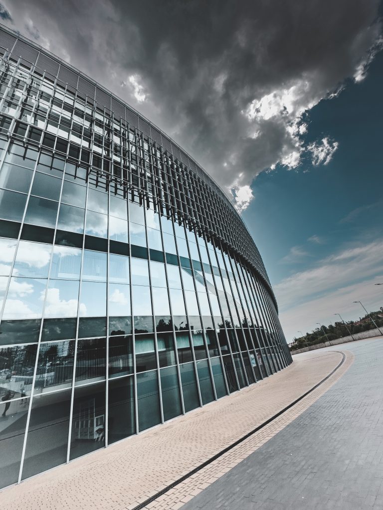 A modern glass-clad corporate building reaching into a sky. Its sleek, reflective facade mirrors the surroundings. The image encapsulates the essence of corporate power and innovation