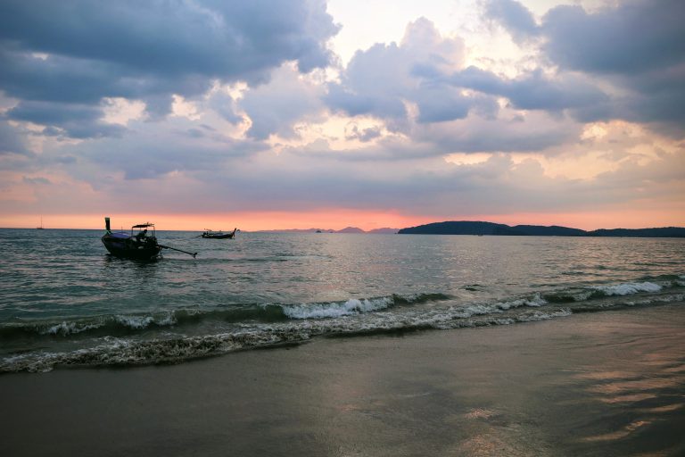 A tranquil scene of a boat resting on a sea shore, bathed in the gentle light sunset, under a sky filled with soft.