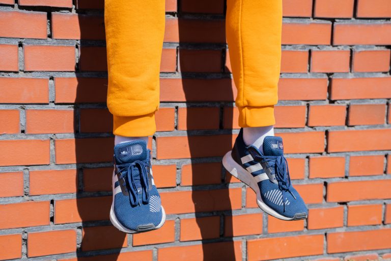 Casually dressed man sitting on a brick wall. He’s wearing trendy sweatpants and stylish sneakers. This photo encapsulates urban lifestyle, street fashion, and modern leisure. Ideal for themes around city life and men’s fashion.