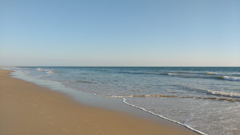 Photo of a beach. Matalasca?as (Huelva – Spain).? Sand on the left, light, shallow surf on the right.