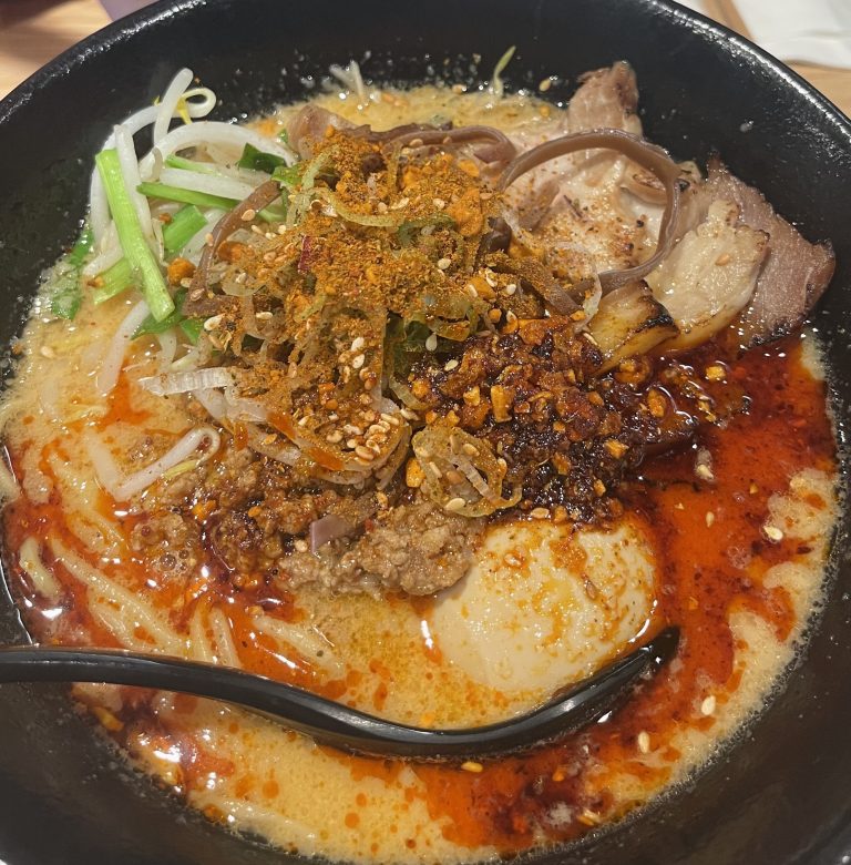 A bowl of spicy ramen with a spoon for broth