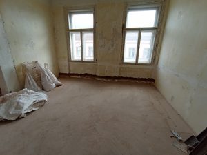 Interior of a room that has dropcloths on the floor, two windows, and nothing on the walls.