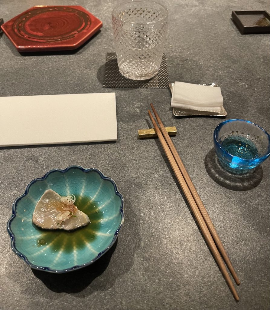 Omakase style sashimi with chopsticks, a shot glass of sake, napkin, and a glass of water