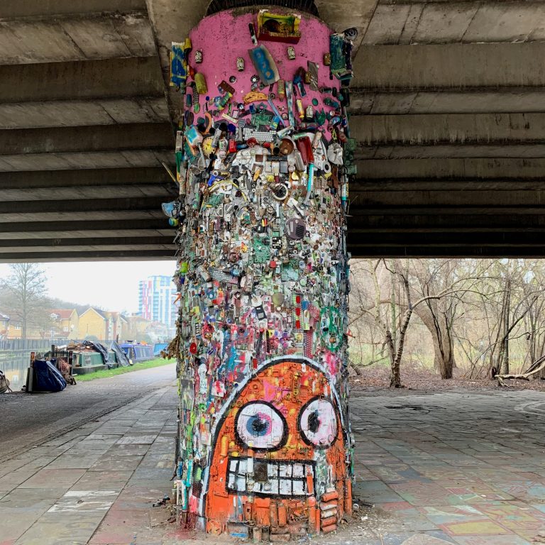 Photo of an underpass where one of the columns is covered in old technology items such as radios, found items, and spray paint